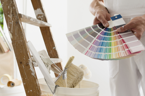 hands of house painter man decorator choose the color using the sample swatch, work of the house to renovate, a wooden ladder with paint brushes and a bucket as a background, close up